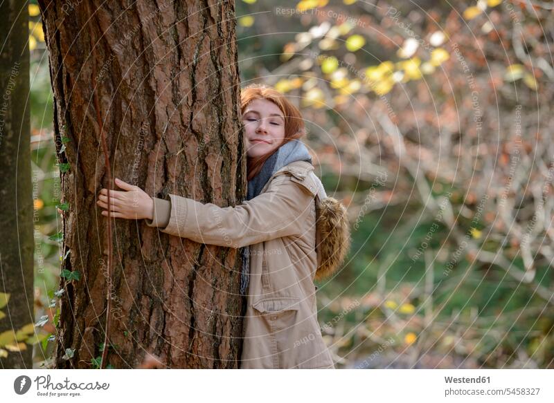 Portrait of smiling teenage girl hugging tree trunk in autumnal forest portrait portraits woods forests autumn forest fall forest autumnally Teenage Girls