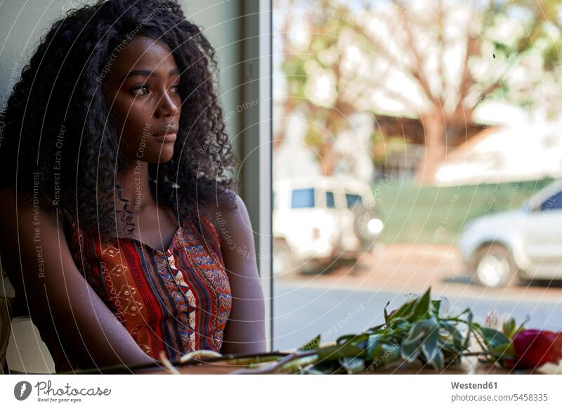 Portrait of young African woman with flowers on the table in a cafe, looking out of window windows Seated sit wait contemplative Reflective thoughtful