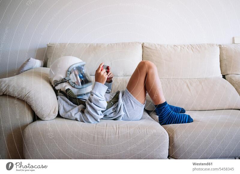 Boy wearing space helmet playing video game while lying on sofa at home color image colour image Spain indoors indoor shot indoor shots interior interior view
