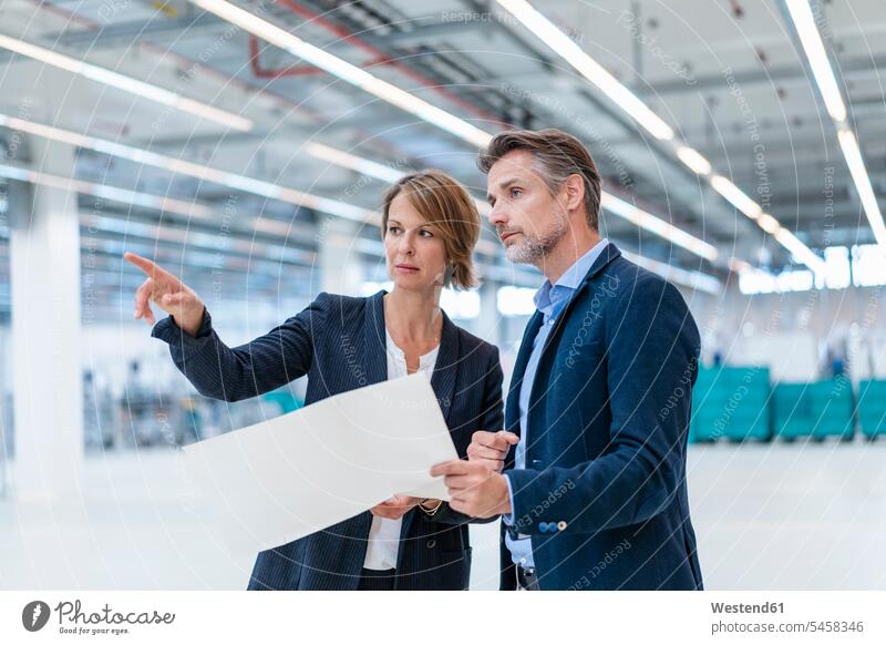 Businessman and businesswoman discussing plan in a factory hall human human being human beings humans person persons caucasian appearance caucasian ethnicity