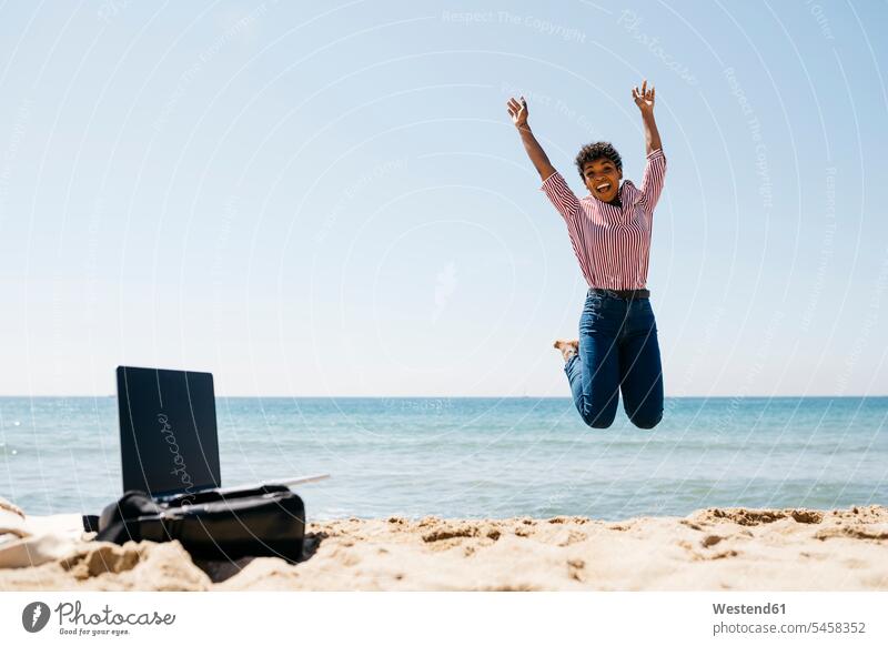 Woman jumping on the beach, laptop on bag human human being human beings humans person persons Mixed Race mixed race ethnicity mixed-race Person 1