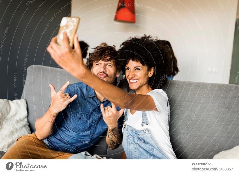 Happy couple sitting on couch taking a selfie Seated Selfie Selfies twosomes partnership couples happiness happy settee sofa sofas couches settees people