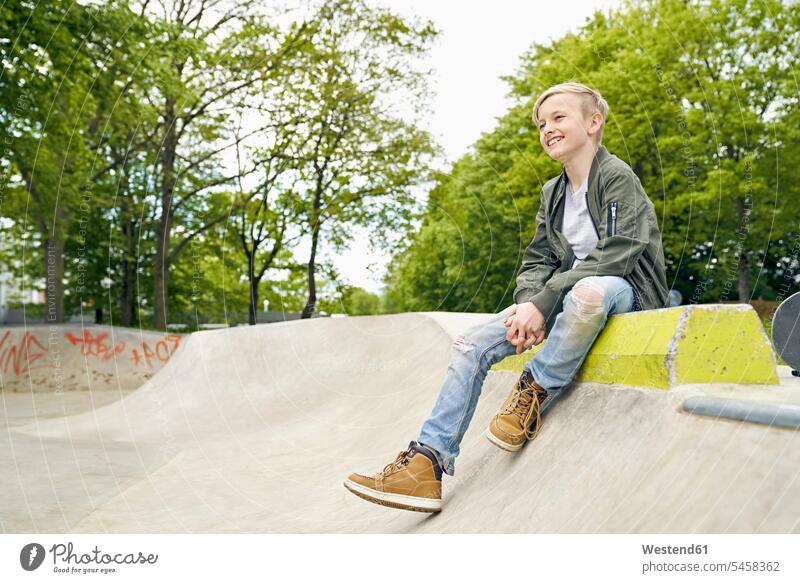 Laughing boy looking to the side in skatepark Skateboard Park skate park sitting Seated leisure free time leisure time looking sideways sideways glance