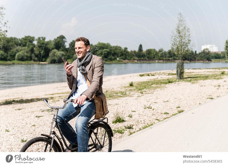 Mature man with bike using smartphone at Rhine riverbank bicycle bikes bicycles Smartphone iPhone Smartphones cyclist men males on the phone call telephoning