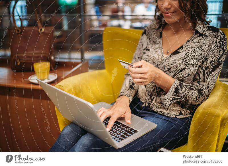 Close-up of young woman sitting in armchair using laptop and credit card human human being human beings humans person persons African black black ethnicity