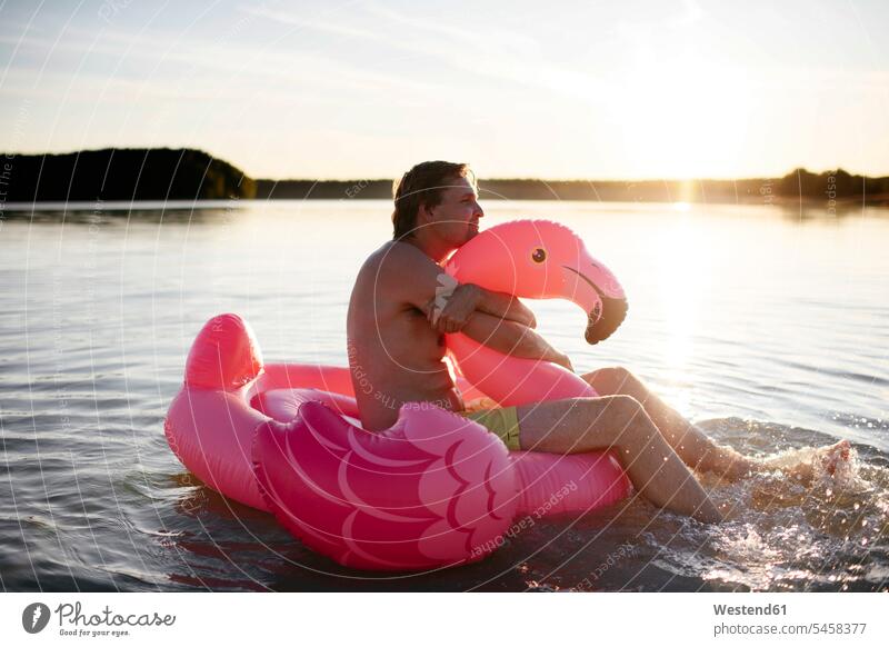 Young man with flamingo pool float on a lake floating tires floating tyre floating tyres relax relaxing smile Seated sit embrace Embracement hug hugging