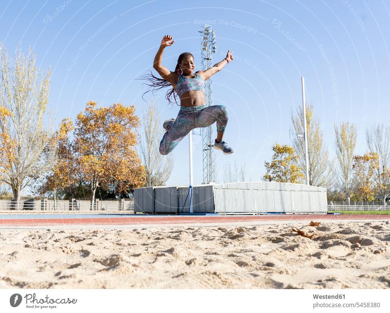 Cheerful sportswoman training for long jump over sand during sunny day color image colour image outdoors location shots outdoor shot outdoor shots daylight shot