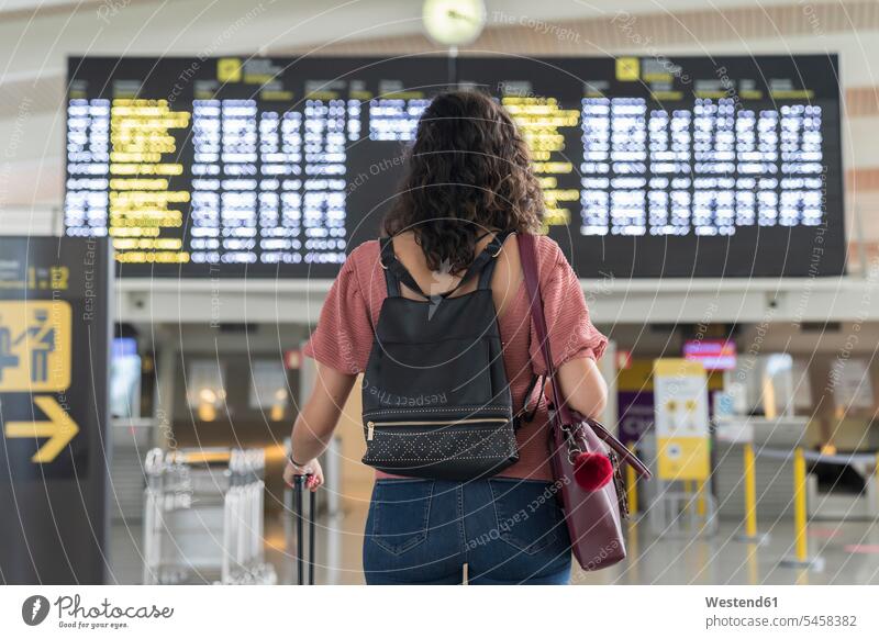 Young woman checking her flight in time board at airport color image colour image indoors indoor shot indoor shots interior interior view Interiors day