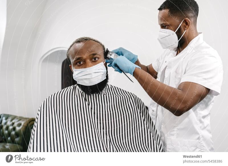 Barber wearing surgical mask and reusable gloves shaving hair of customer human human being human beings humans person persons client clientele clients