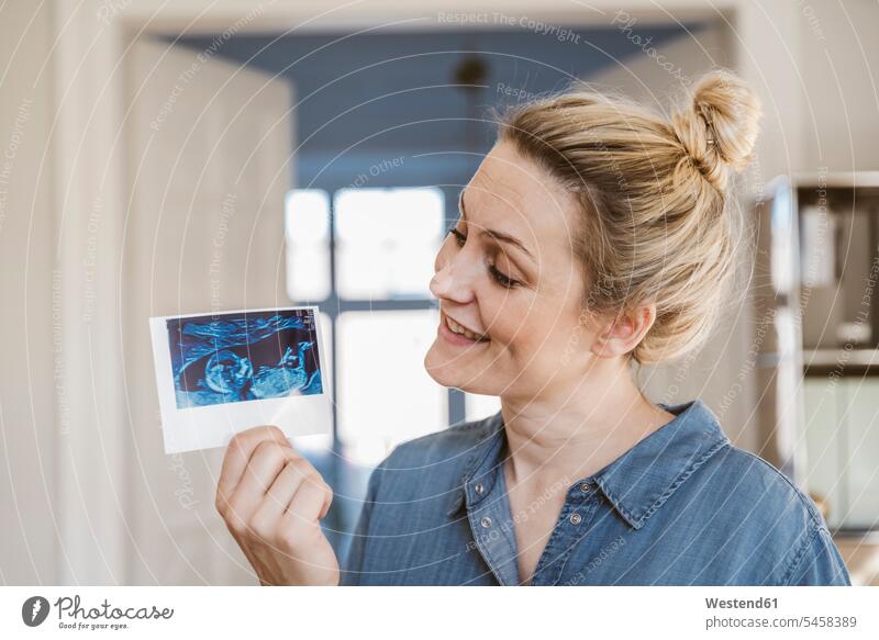 Pregnant woman holding ultrasound image at home images picture pictures smile delight enjoyment Pleasant pleasure happy Contented Emotion pleased Pregnant Woman