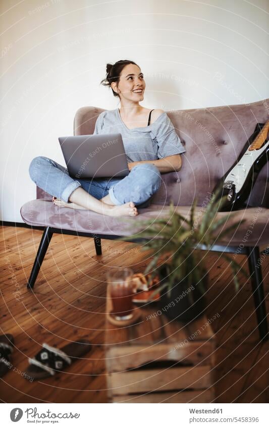Portrait of smiling young woman sitting on couch at home with laptop human human being human beings humans person persons adult grown-up grown-ups grownup