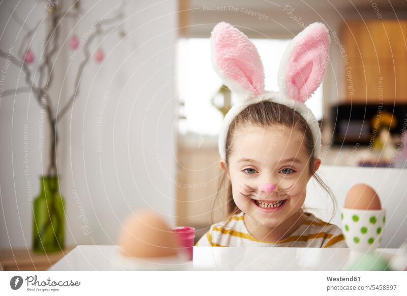 Portrait of smiling girl with bunny ears sitting at table with Easter eggs females girls Rabbit Ears Bunny Ear Bunny Ears costume rabbit ears portrait portraits