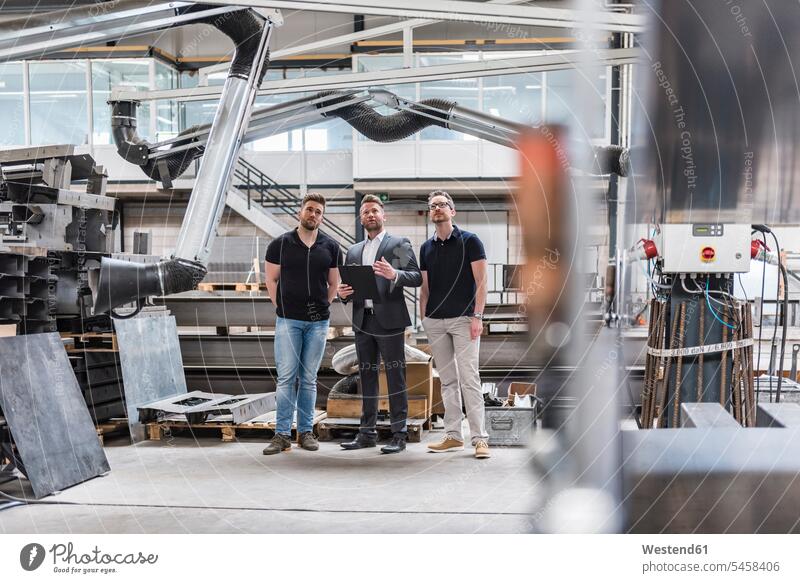 Three men standing and talking on factory shop floor production hall speaking man males factories Adults grown-ups grownups adult people persons human being