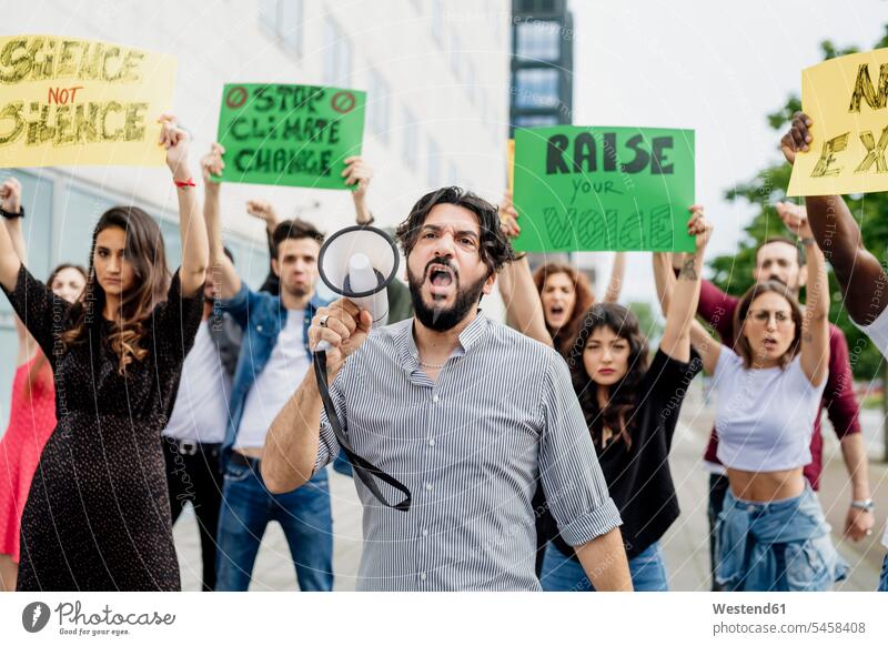 Man shouting through megaphone while protesting with people on street color image colour image casual clothing casual wear leisure wear casual clothes