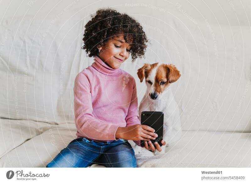 Portrait of smiling little girl sitting on the couch with her dog taking selfie with smartphone human human being human beings humans person persons 1