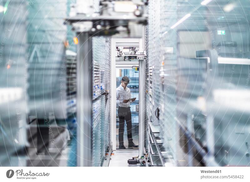 Businessman using digital tablet while standing in factory seen through glass caucasian caucasian appearance caucasian ethnicity european White - Caucasian