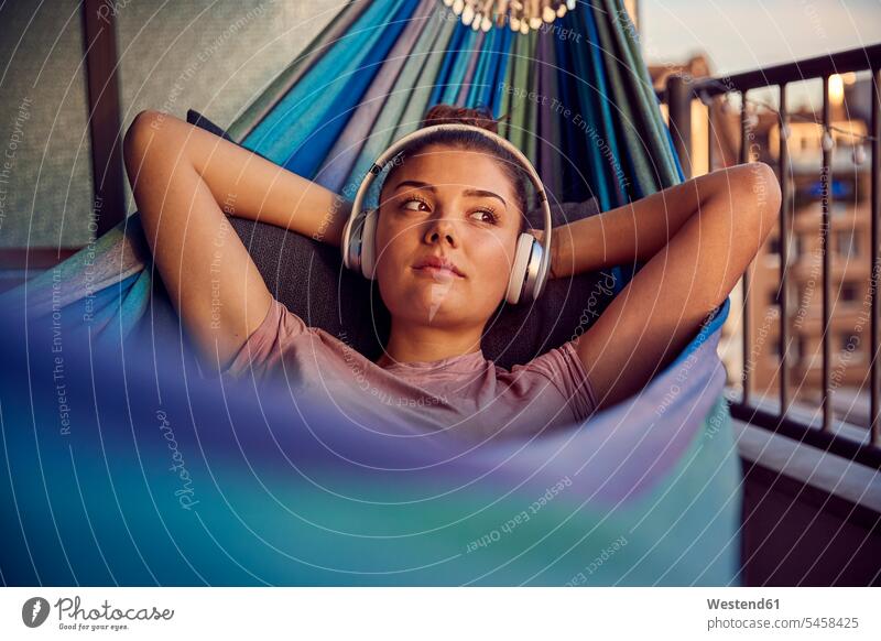 Portrait of young woman lying on hammock on balcony listening music with headphones hammocks headset hear in the evening Late Evening relax relaxing relaxation