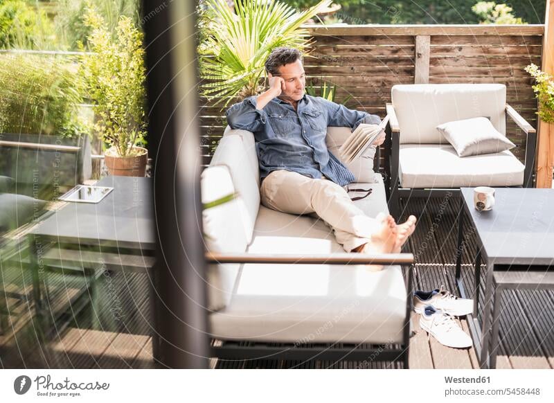 Confident man relaxing on the terrace, reading book books couches settee settees sofa sofas Seated sit free time leisure time concentrate concentrated