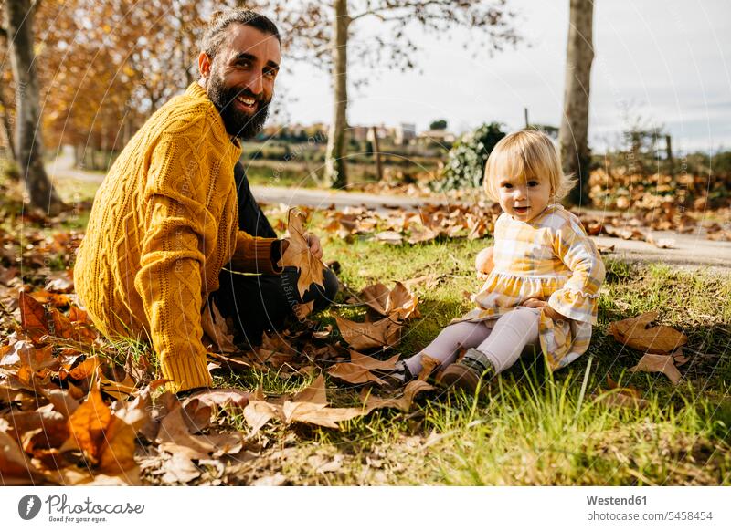 Father and daughter sitting on meadow with autumn leaves, morning day in the park in the morning Leaf Leaves Meadow Meadows father fathers daddy dads papa