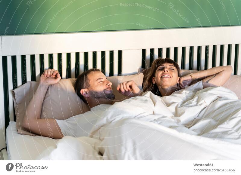 Smiling couple waking up slowly while lying on bed at home color image colour image indoors indoor shot indoor shots interior interior view Interiors morning