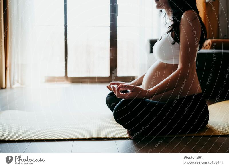 Pregnant woman meditating while sitting on exercise mat at home color image colour image indoors indoor shot indoor shots interior interior view Interiors day