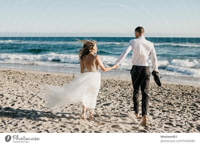 Rear view of bride and groom running on the beach Celebration Event Celebrations Ceremonies Ceremony Festivities Festivity getting married Marriage marrying