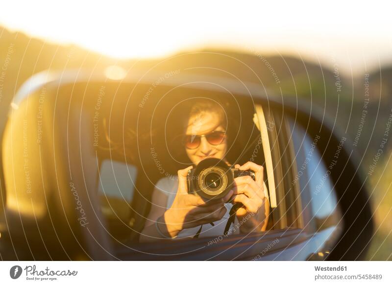 Young woman taking picture of her mirror image in her car females women summer summer time summery summertime automobile Auto cars motorcars Automobiles mirrors