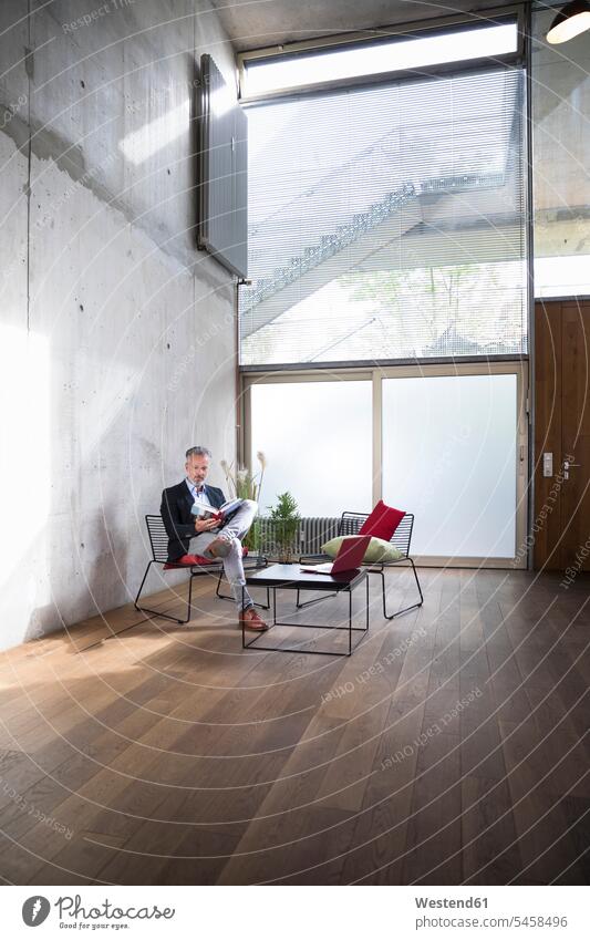 Businessman sitting in a loft at concrete wall reading book concrete walls Business man Businessmen Business men books Seated lofts business people