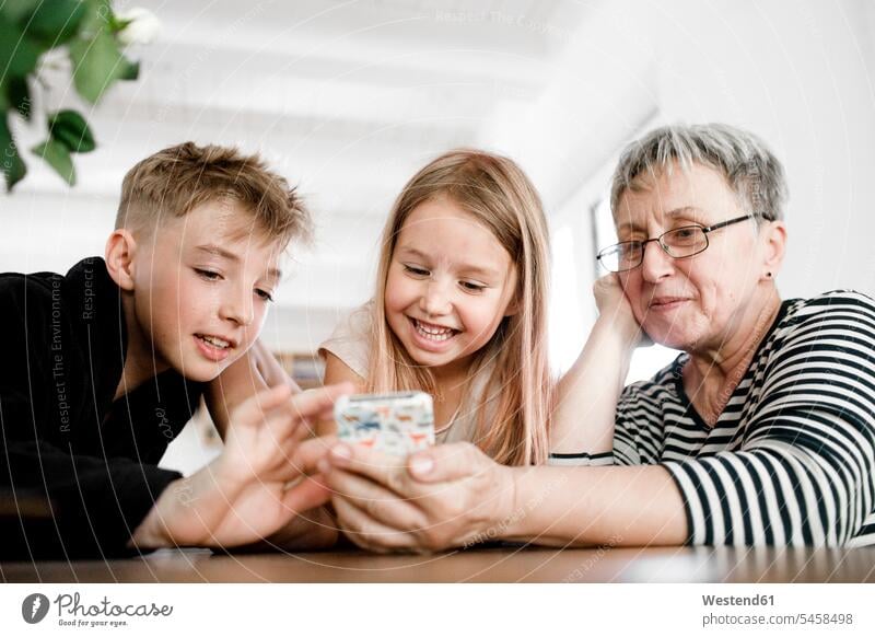 Happy grandmother and grandchildren using cell phone at home Knowledge Table Tables explaining playing domestic life domestic scene happiness happy enjoying