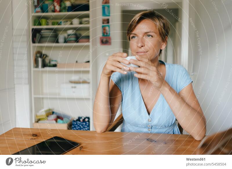 Woman sitting at table at home with cup of coffee Coffee Cup Coffee Cups woman females women Seated Table Tables Drink beverages Drinks Beverage food and drink
