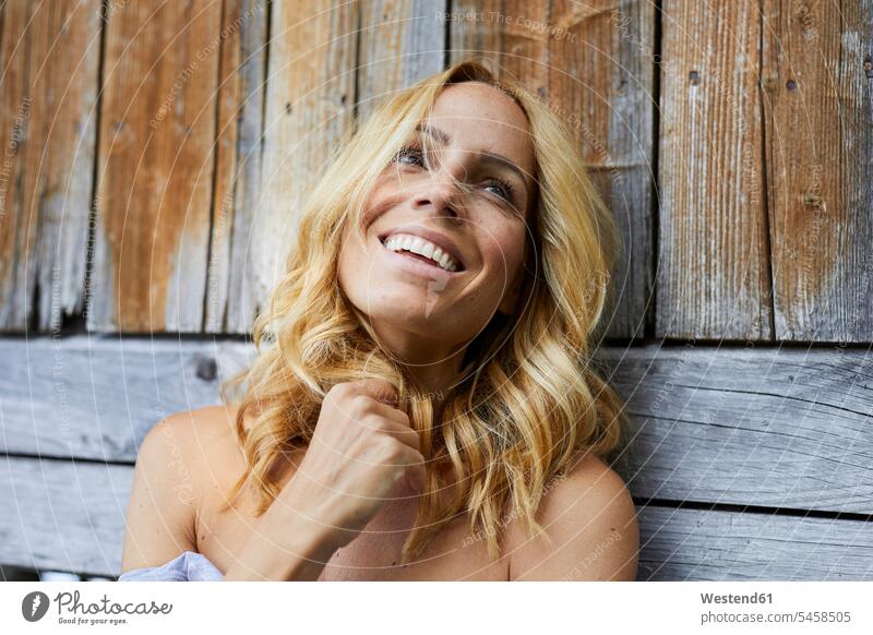 Portrait of happy blond woman in front of wooden wall blond hair blonde hair freckles freckled smiling smile females women wooden walls people persons