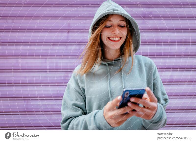 Portrait of young blonde woman with green hoodie and purple background telecommunication phones telephone telephones cell phone cell phones Cellphone mobile