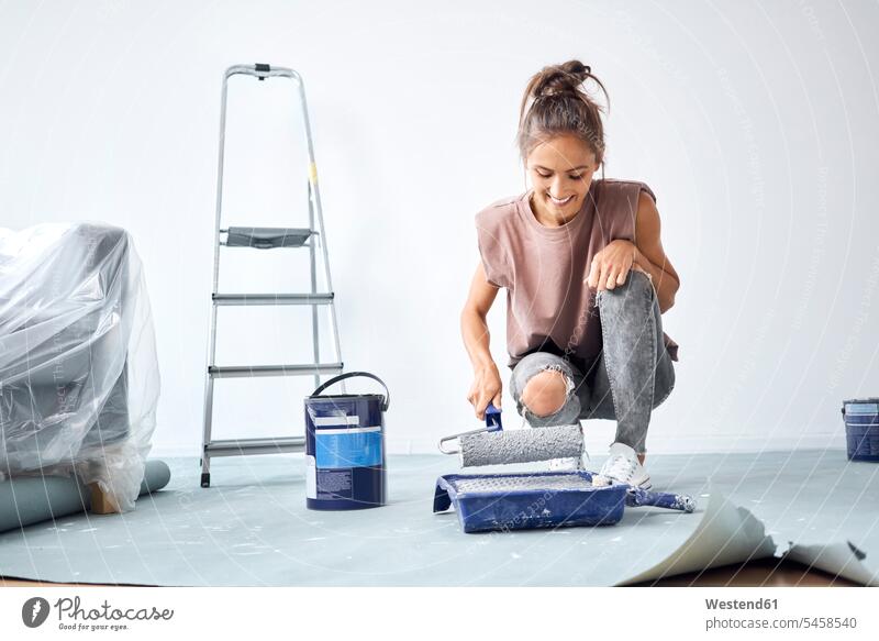 Smiling woman holding paint roller while crouching at home color image colour image indoors indoor shot indoor shots interior interior view Interiors day