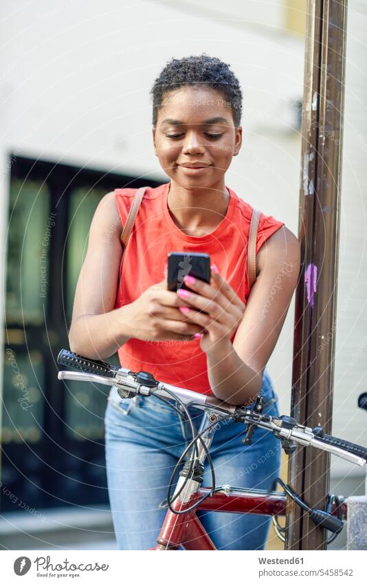 Portrait of smiling young woman leaning on handle bar of bicycle looking at cell phone human human being human beings humans person persons African black