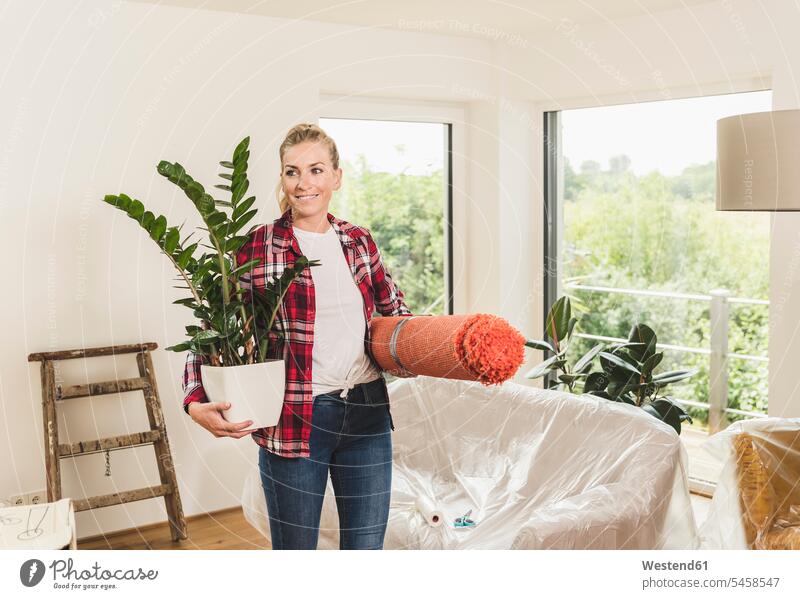Woman moving into new home carrying carpet and potted plant human human being human beings humans person persons celibate celibates singles solitary people