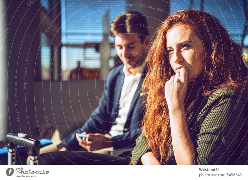 Thoughtful businesswoman sitting with man at airport departure area color image colour image indoors indoor shot indoor shots interior interior view Interiors