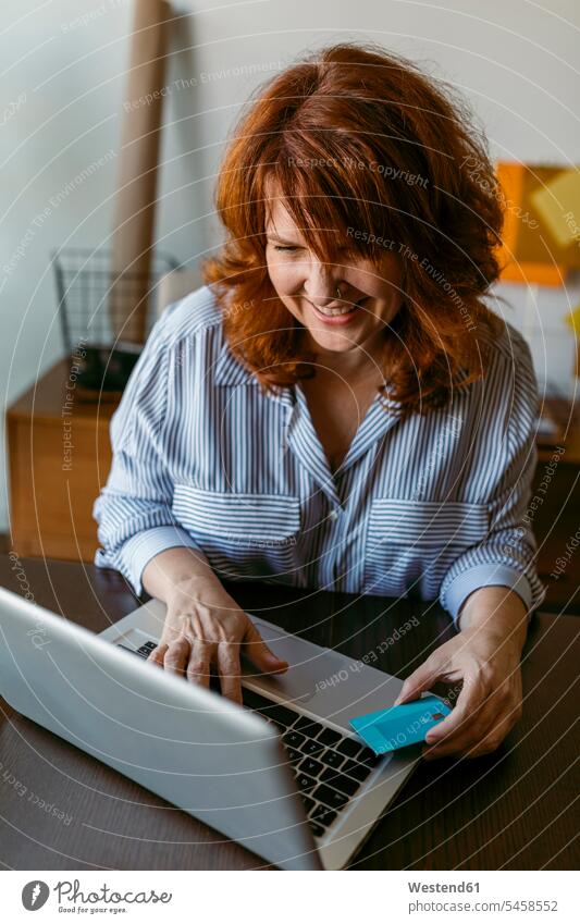 Smiling woman doing online shopping on laptop while sitting at home color image colour image indoors indoor shot indoor shots interior interior view Interiors