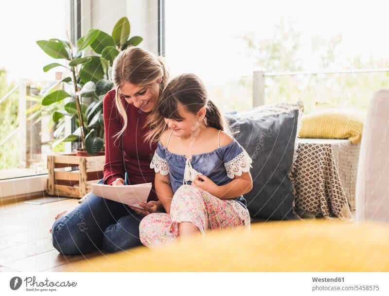 Mother helping daughter with homework at home windows pencil pencils pens learn smile write Seated sit relax relaxing relaxation Contented Emotion pleased