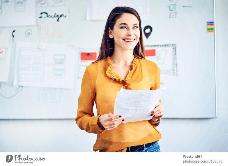 Smiling businesswoman with papers standing at whiteboard leading a presentation office offices office room office rooms smiling smile presentations Conducting