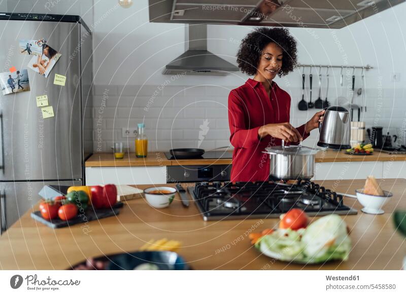 Woman standing in kitchen, preparing food Afro European Ethnicity Food Preparation black hair black-haired black hairs curly hair curls Cooking Pot Pots