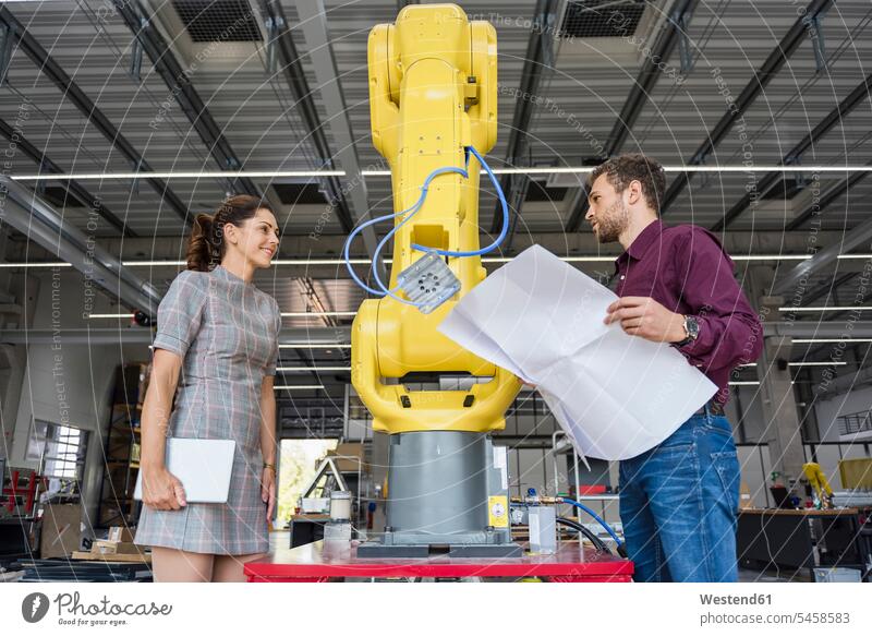 Businessman and woman having a meeting in front of industrial robots in a high tech company team maintenance manufacturing tablet digitizer Tablet Computer