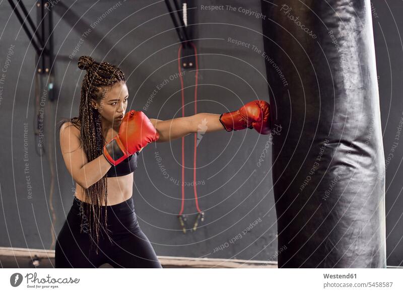 Female boxer wearing red gloves practicing boxing drill on punching bag in gym color image colour image South Africa indoors indoor shot indoor shots interior