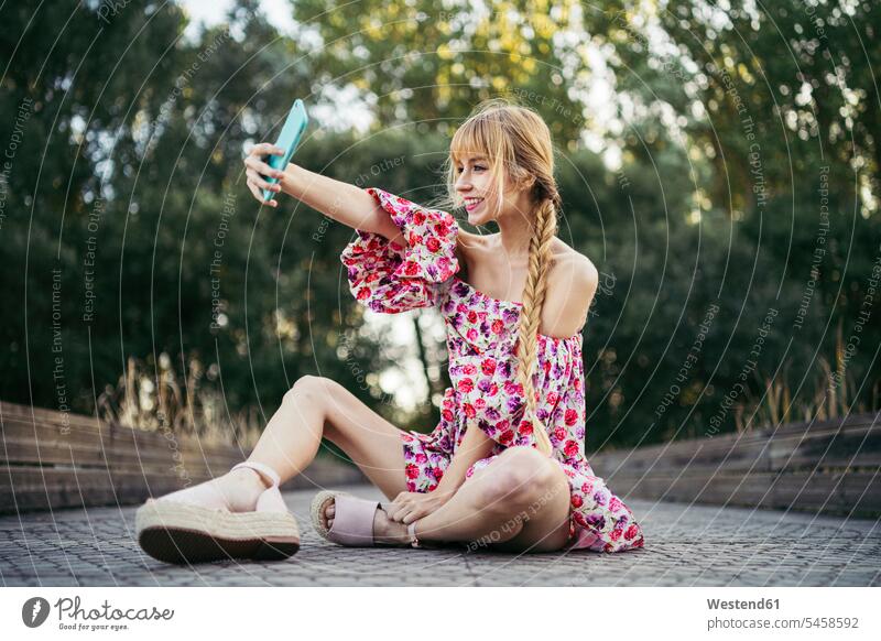 Portrait of smiling young woman sitting on boardwalk in summer taking selfie with smartphone cell phone cell phones Cellphone mobile mobile phones mobiles smile