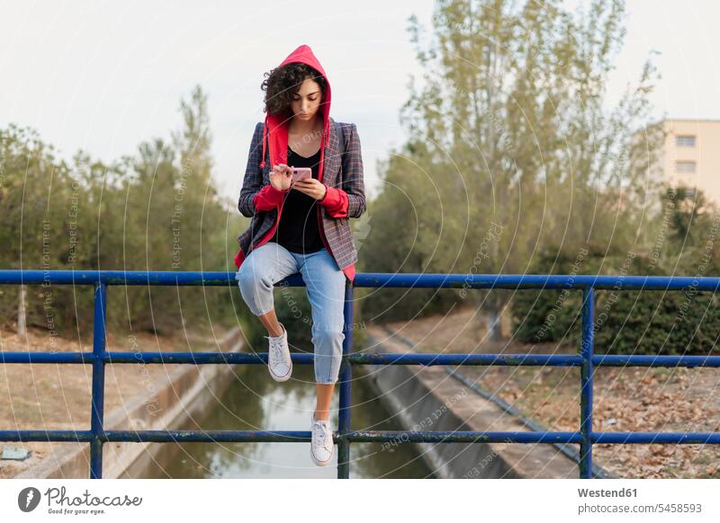 Young woman sitting on railing using mobile phone human human being human beings humans person persons caucasian appearance caucasian ethnicity european 1