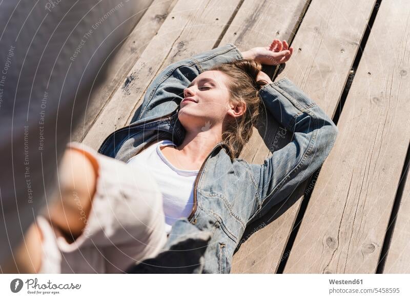 Relaxed young woman lying on wooden boards in sunshine females women relaxed relaxation sunlight Sunlit wooden panel wooden panels laying down lie lying down