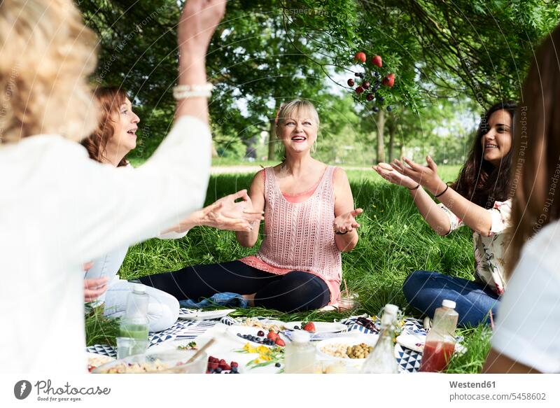 Happy women throwing berries in the air at a picnic in park happiness happy female friends Picnic picnicking parks woman females Berry Berries mate friendship