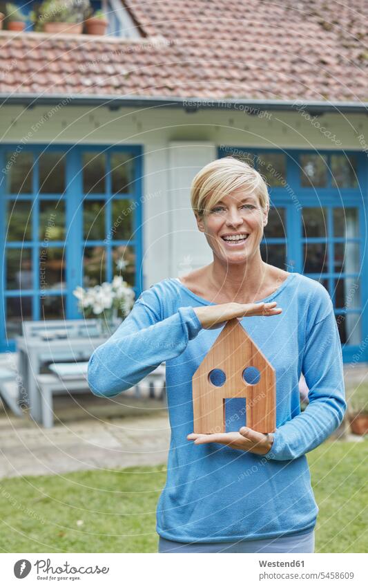 Portrait of smiling woman standing in front of her home holding house model portrait portraits models smile females women houses Adults grown-ups grownups adult
