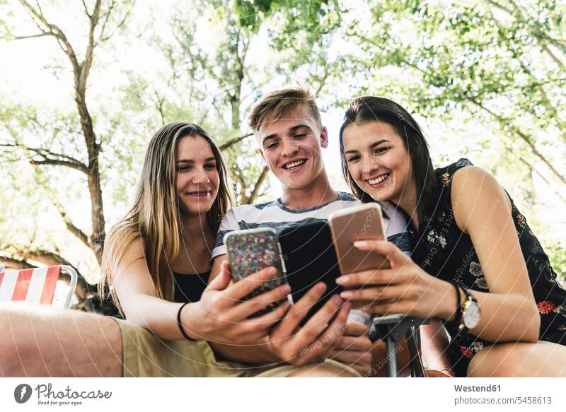 Three happy friends looking at cell phones outdoors happiness mobile phone mobiles mobile phones Cellphone mate eyeing group of people Group groups of people