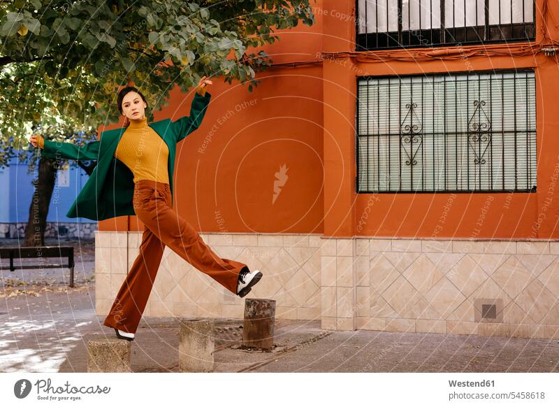Beautiful woman wearing green jacket climbing on bollard in city color image colour image Spain casual clothing casual wear leisure wear casual clothes