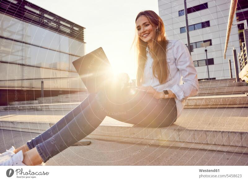 Young businesswoman using laptop while sitting on staircase in city color image colour image outdoors location shots outdoor shot outdoor shots sunset sunsets